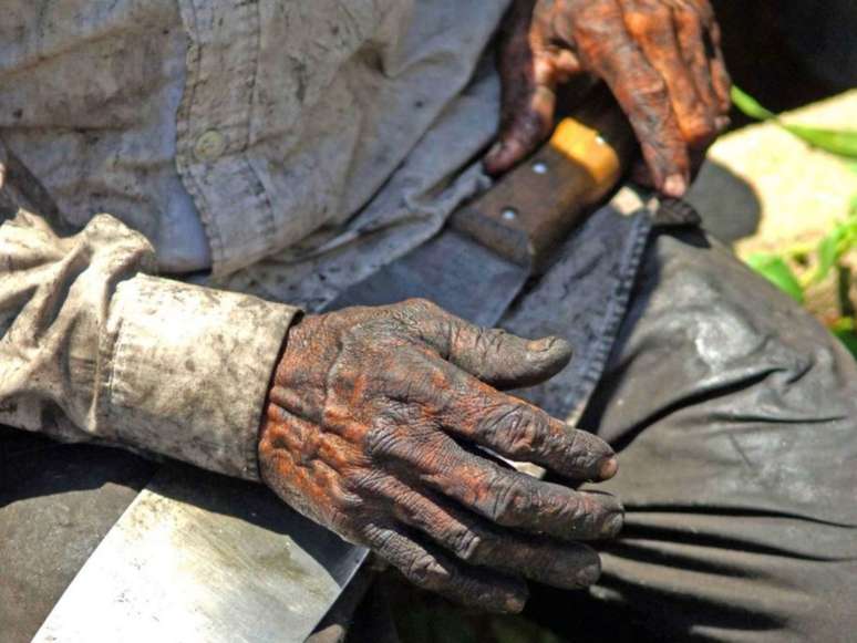 A imagem mostra as mãos de um homem negro segurando um facão usado para cortar cana-de-açúcar.