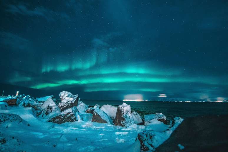 O azul da aurora boreal ilumina a neve e as águas em Reykjavik