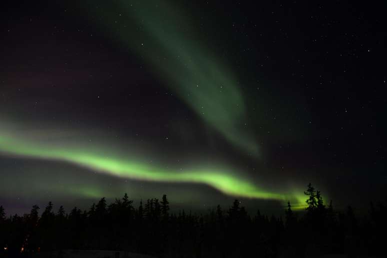 Na noite escura de Yellowknife, luzes esverdeadas agitam o céu