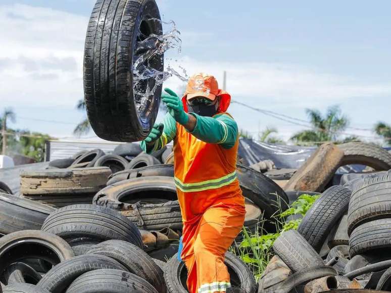Imagem mostra um agente de limpeza municipal jogando um pneu com água acumulada para eliminar focos de transmissão da dengue.