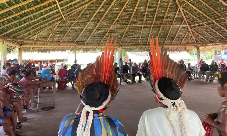 Imagem ilustrativa mostra duas lideranças indígenas à frente de reunião em aldeia.