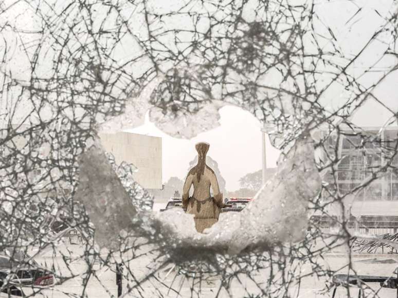 Imagem mostra a escultura da Justiça, de costas, através dos estilhaços de vidro ocasionados pelos atos democráticos contra as sedes dos Três Poderes.