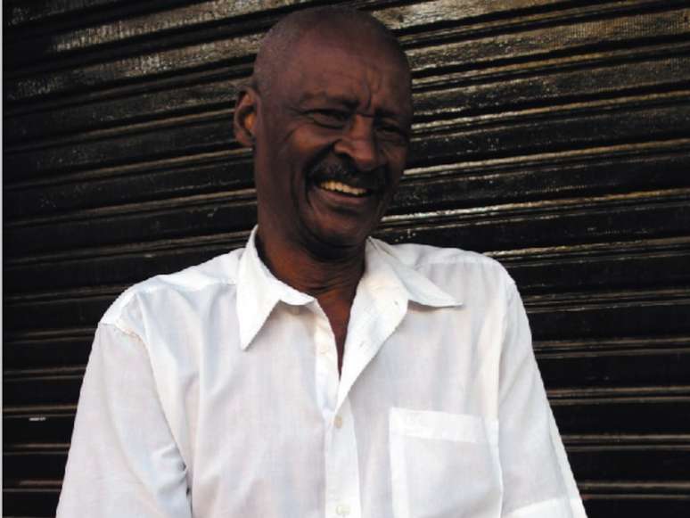 Imagem mostra Seu Carlão do Peruche, um idoso negro com uma camisa social branca.