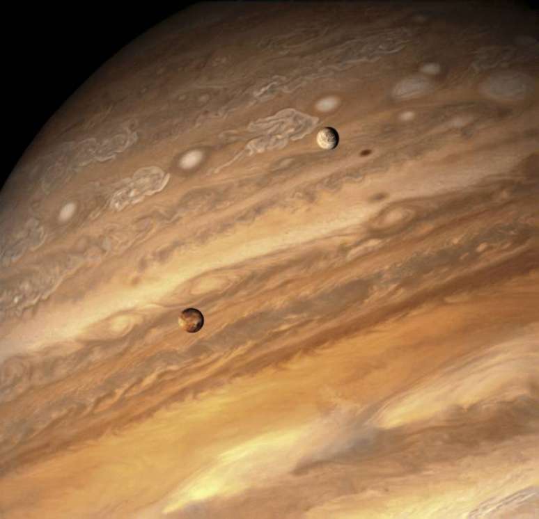 À esquerda, a lua Io, avermelhada, orbitando Júpiter em um registro do final de 2023 feito pelo satélite Juno.