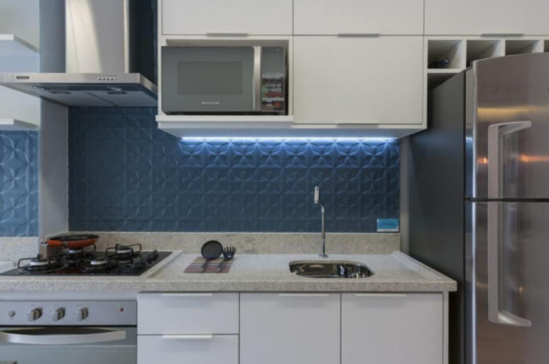 7. Cerâmica para cozinha: revestimento azul na parede, móveis planejados em marcenaria branca, bancada de granito com cooktop preto e coifa de inox – Projeto: Adriana Fontana