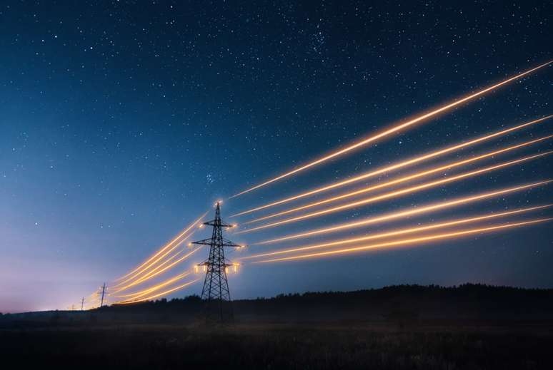 Torres de transmissão de eletricidade com fios laranjas brilhando contra o céu noturno