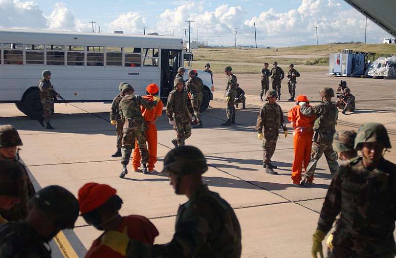 Fuzileiros navais dos EUA transportam vários prisioneiros do avião que os trouxe do Afeganistão para um ônibus que os levaria para a prisão da base de Guantánamo