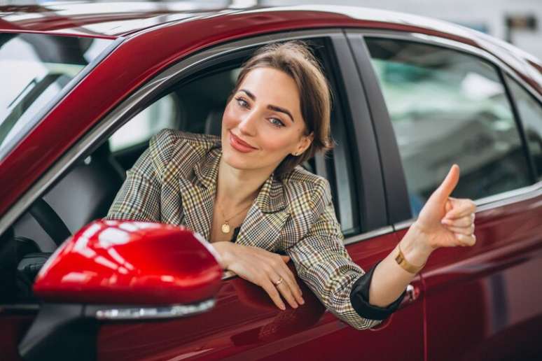 Imagem mostra mulher em carro vermelho com seguro de carro. 