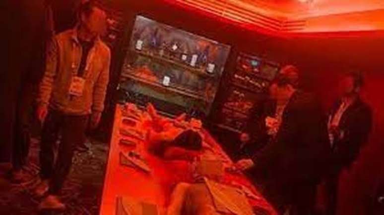 A imagem mostra um grupo de homens no quarto laqueado de vermelho do hotel cinco estrelas Mandrake, no centro de Londres, com um homem e uma mulher parcialmente nus, deitados imóveis na mesa à sua frente.