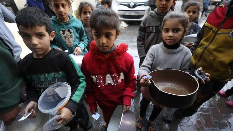 Crianças com potes e panelas vazias esperam enquanto equipes de ajuda humanitária distribuem alimentos em Gaza