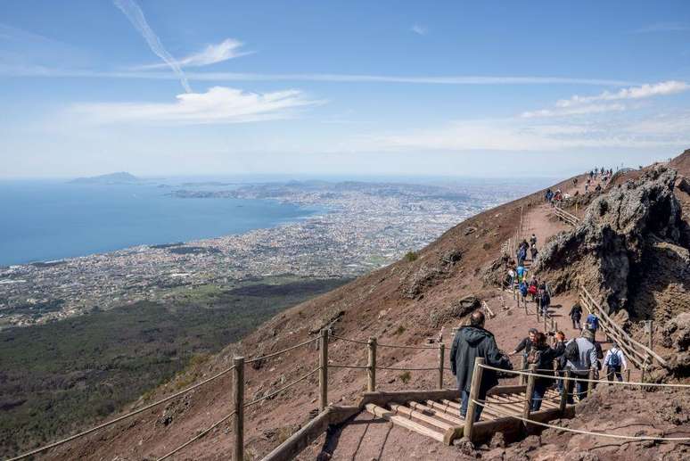 Turistas subindo pela trilha no Monte Ves&uacute;vio com vista para N&aacute;poles
