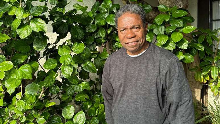 Paulinho sorrindo enquanto posa para foto em um ambiente com plantas