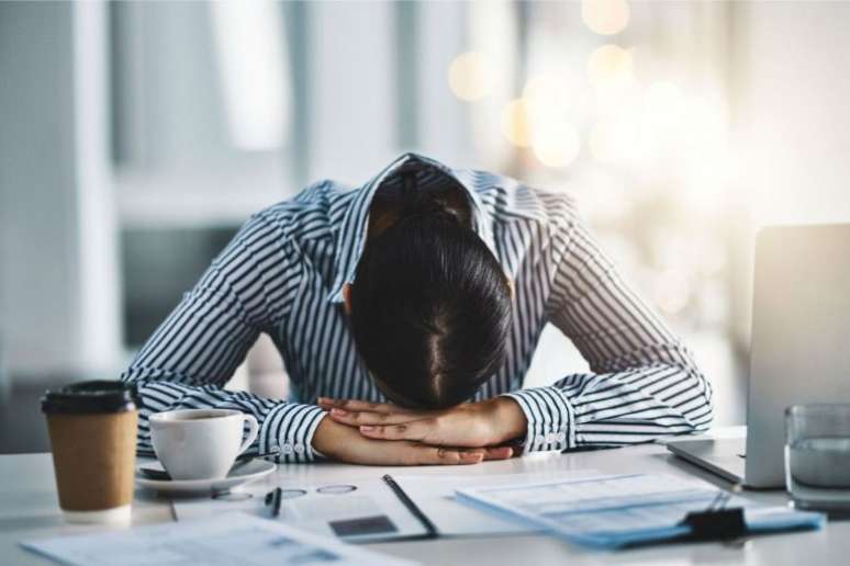 Pessoa com a cabeça deitada na mesa, representando o esgotamento mental causado pelo burnout. 