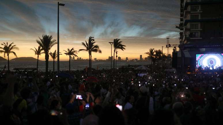 Milhares de visitantes e pessoas locais usam seus celulares para fotografar o fenômeno em Mazatlán, no México. A sombra causada pelo eclipse escureceu o local