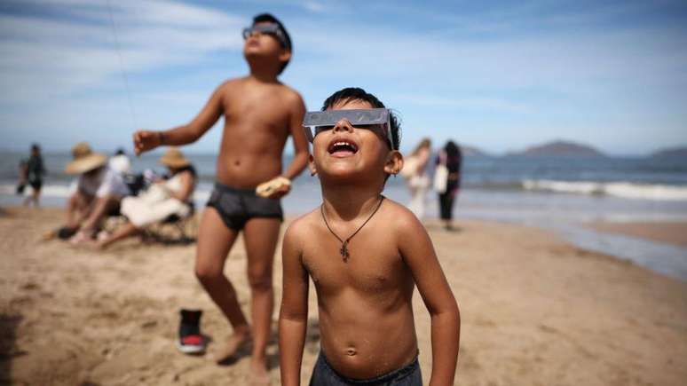 Crianças pausaram suas brincadeiras na praia para assistir ao início do eclipse em Mazatlán, México