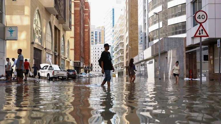 Pessoas caminham pelas ruas alagadas em decorrência das enchentes causadas pelas fortes chuvas em Dubai