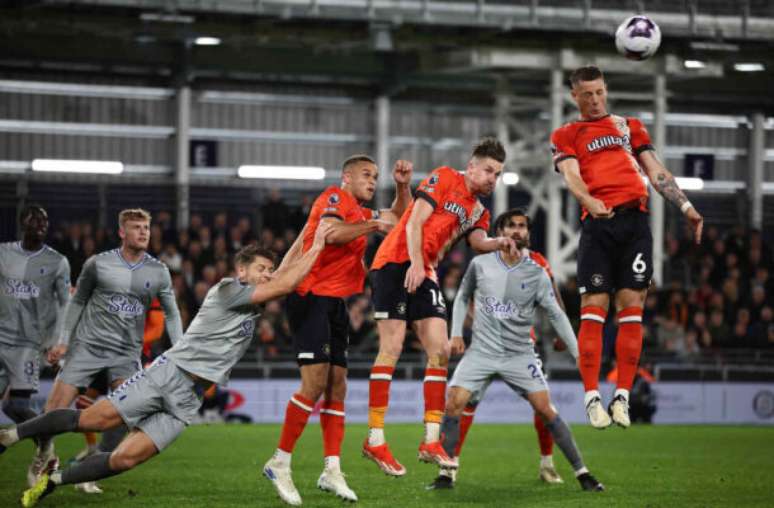 Henry Nicholls/AFP via Getty Images - Legenda: Jogadores de Luton Town e Everton em disputa de bola na Premier League -