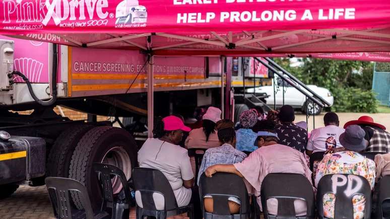 Mulheres aguardam ao lado de van rosa de campanha para realizar exame para detecção precoce de câncer