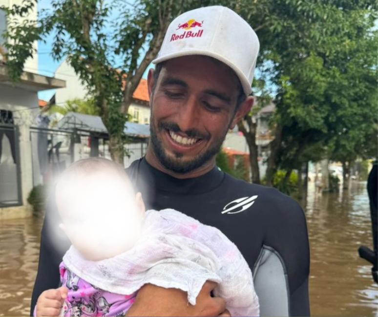 Lucas Chumbo sorridente ao lado de uma bebê resgatada no Rio Grande do Sul. 