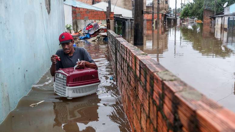 Homem deixa sua casa com gata de estimação no bairro Humaitá em Porto Alegre no domingo (12/5)