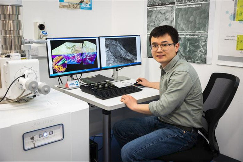 Zixiao Yang junto às imagens obtidas da pele do psitacossauro, em laboratório da Universidade de Cork (Imagem: Ruben Tapia/UCC TV)