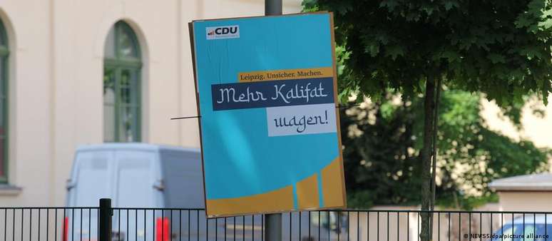 No cartaz falso, abaixo do slogan adulterado, uma inscrição com letras curvas diz: "Mehr Kalifat wagen!" (Ouse mais califado).