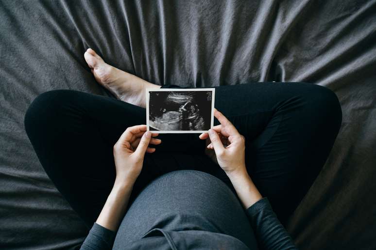 Uma pessoa grávida, segurando imagem de ultrassom. 