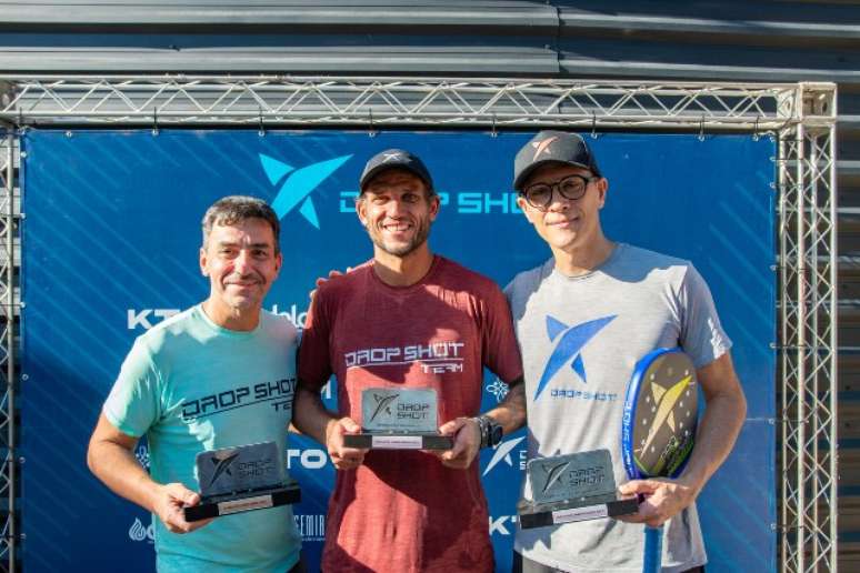 Rafael Moura, de vermelho, ao centro com o troféu do Beach Tennis com Pablo Oliveira à direita, de cinza. À esquerda, Ricardo Aloise /