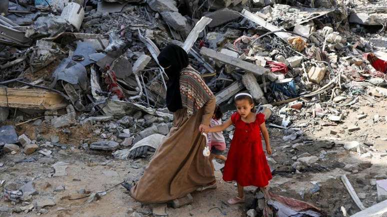 Mãe e filha caminham sobre ruínas em Gaza