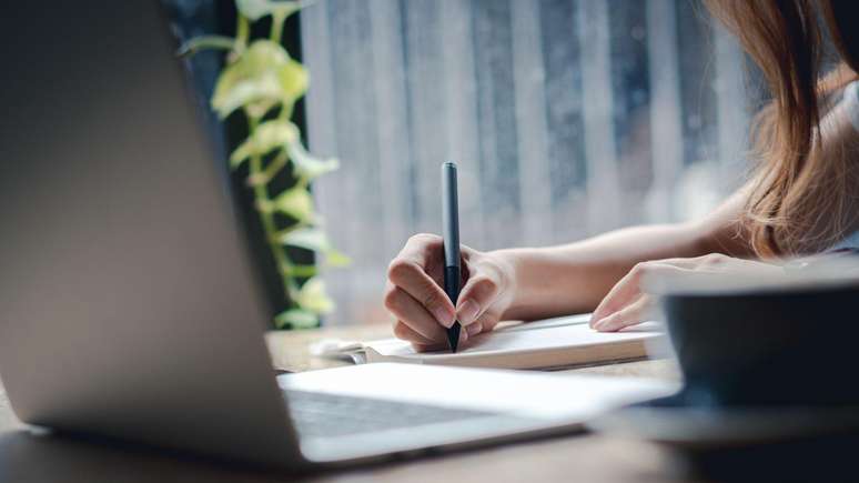 Mulher escrevendo em caderno com laptop na frente