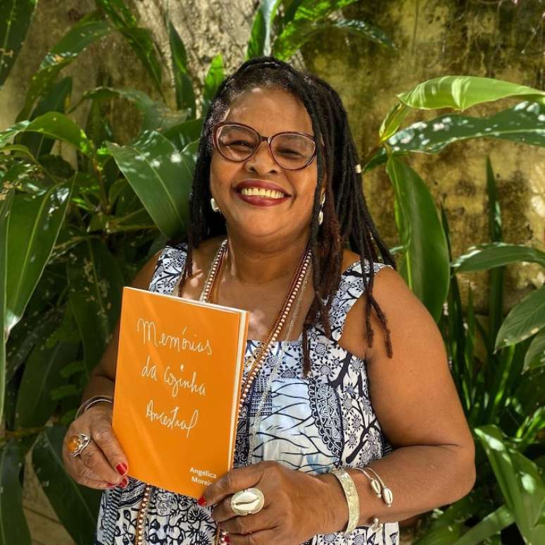 A escritora Angélica Moreira segura seu livro "Memórias da Cozinha Ancestral"