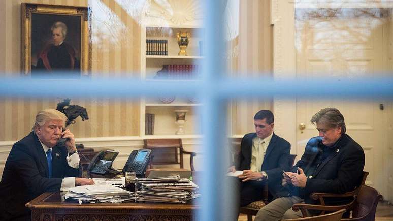Steve Bannon sentado em frente ao então presidente Donald Trump e ao general Michael Flynn no Salão Oval da Casa Branca em 2017