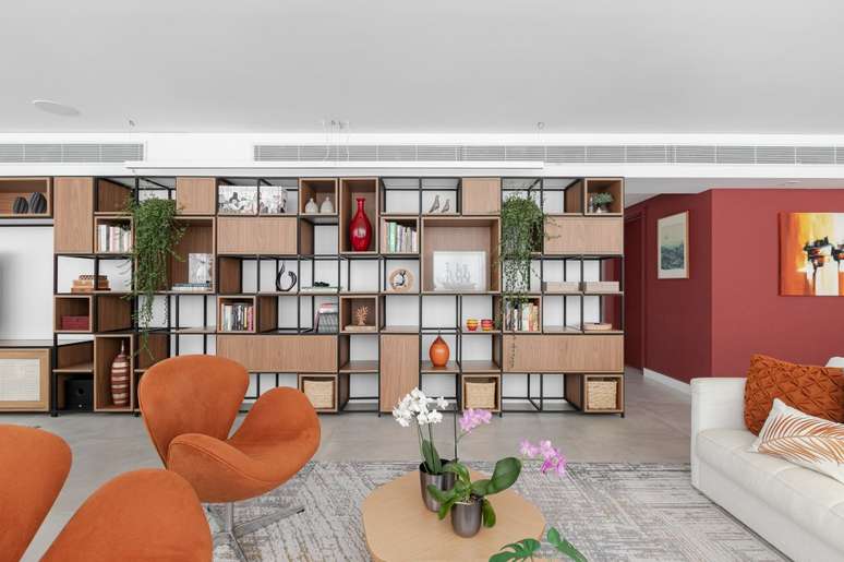 Reforma em ap&ecirc; transforma varanda das su&iacute;tes em sala &iacute;ntima aconchegante. Projeto de atelier C2H.a. Na foto, sala, estante com nichos, poltronas laranjas.