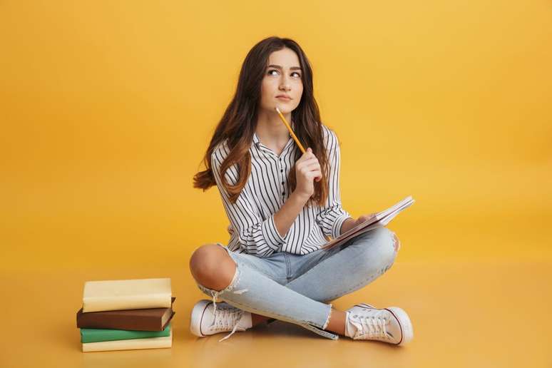 Jovem estudando com livros e caderno na mão.