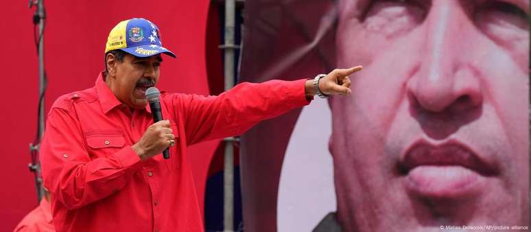 Nicolás Maduro em frente a um cartaz que mostra Hugo Chávez, seu antigo padrinho político. Chavismo conquistou o poder em 1999. Vinte e cinco anos de regime arruinaram economia e levaram milhões a deixar país