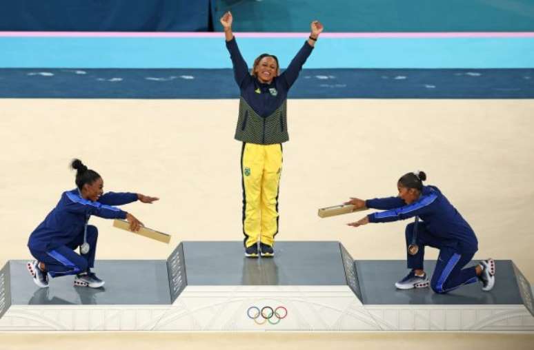 O mito Simone Biles (prata) e a também americana Jordan Chiles (bronze) reverenciam Rebeca Andrade. Afinal, a brasileira leva ouro no solo