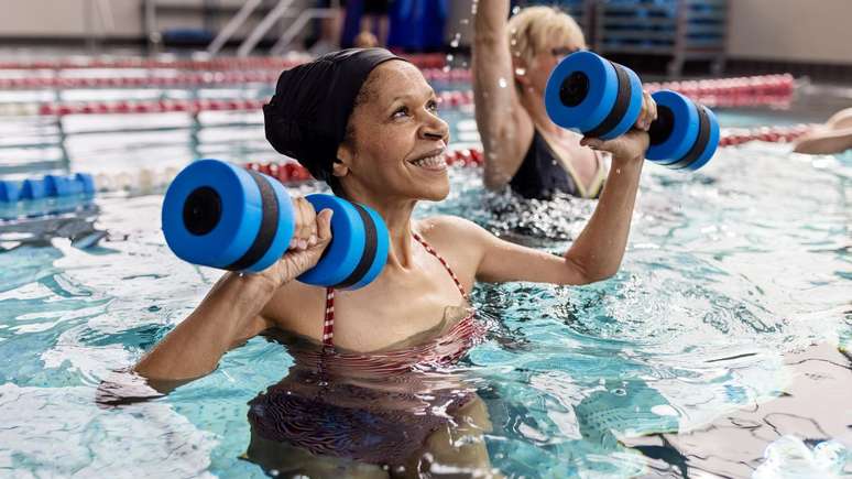 Mulher idosa levantando pesos dentro de uma piscina