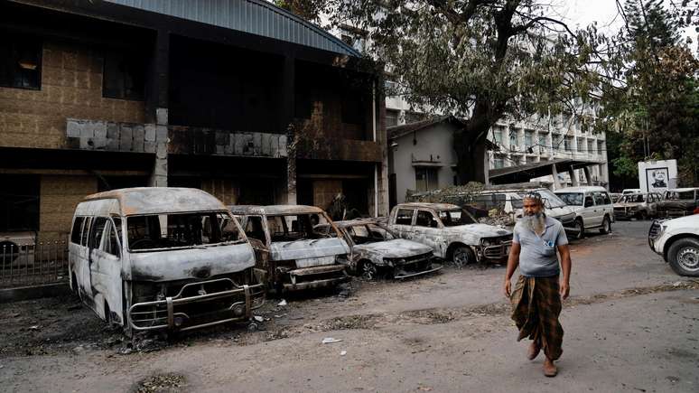 Um homem passa por veículos danificados que foram incendiados durante protestos de estudantes contra as cotas de empregos do governo