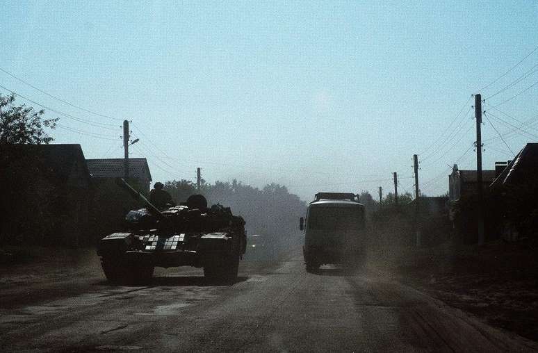 Um ônibus civil passa por um tanque ucraniano em uma estrada na vila de Yunakivka, a 9 quilômetros da fronteira com a Rússia