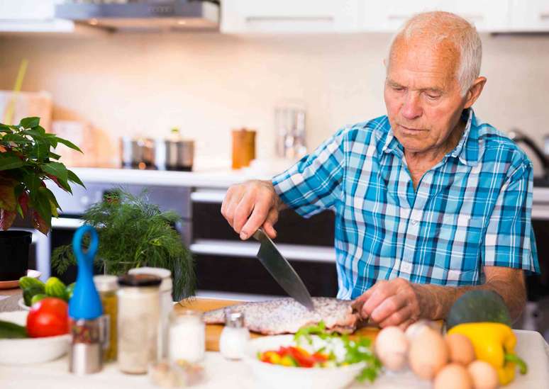 Um homem mais velho na cozinha prepara um peixe para cozinhar.