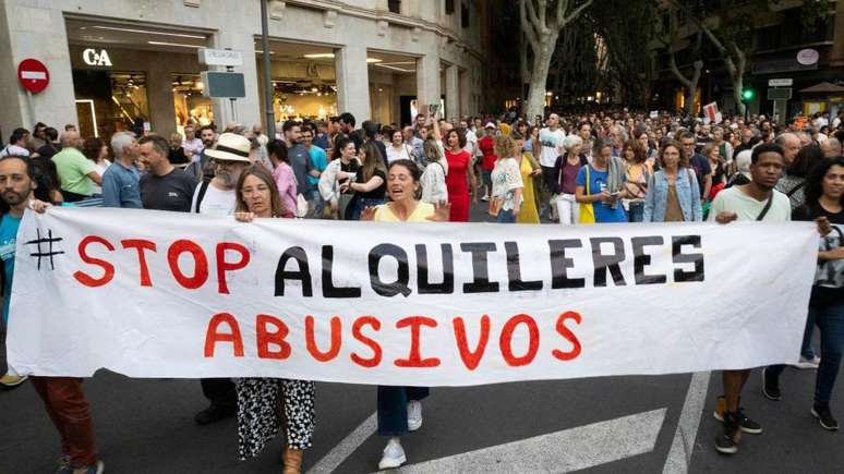 Faixa em espanhol pede o fim de 'aluguéis abusivos' em protesto por moradia digna