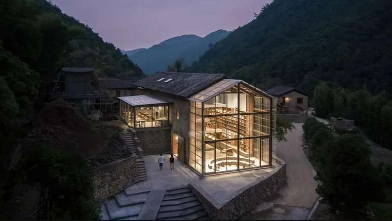 Vista externa de casa de vidro iluminada, aparentemente ao entardecer