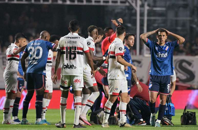 Jogadores de São Paulo e Nacional (URU) exibem tensão posteriormente a queda de Izquierdo em campo –