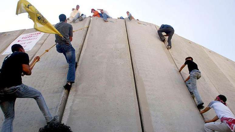 Palestinos escalam o muro que os separa de Israel durante uma marcha pela paz na cidade de Abu Dis, na Cisjordânia