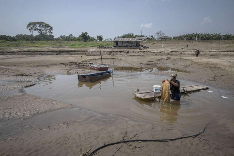 Mulher lava roupas em uma poça no que sobrou de água do rio Costa do Barroso, em Manaquiri, Amazonas