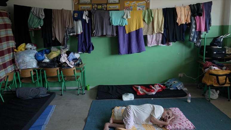 A família de Um Ahmad dorme em colchões no chão enquanto penduram roupas pela sala de aula