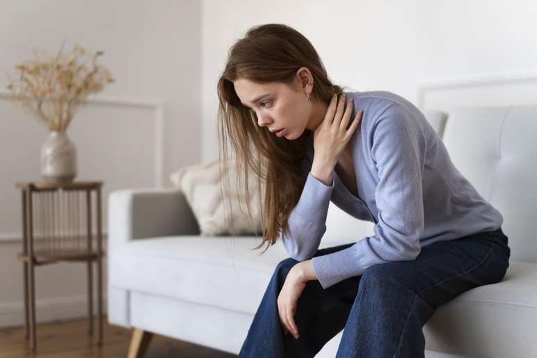 Mulher com as mãos na região do pescoço e semblante de dor