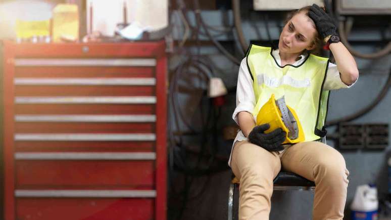 Mulher estressada trabalhando em uma f&aacute;brica, com &oacute;culos de prote&ccedil;&atilde;o e capacete.