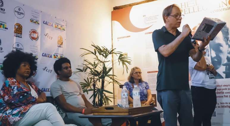 Wesley Barbosa, sentado, acompanha Pedro Cardoso lendo seu romance Viela Ensanguentada na Flip, em Paraty (RJ).