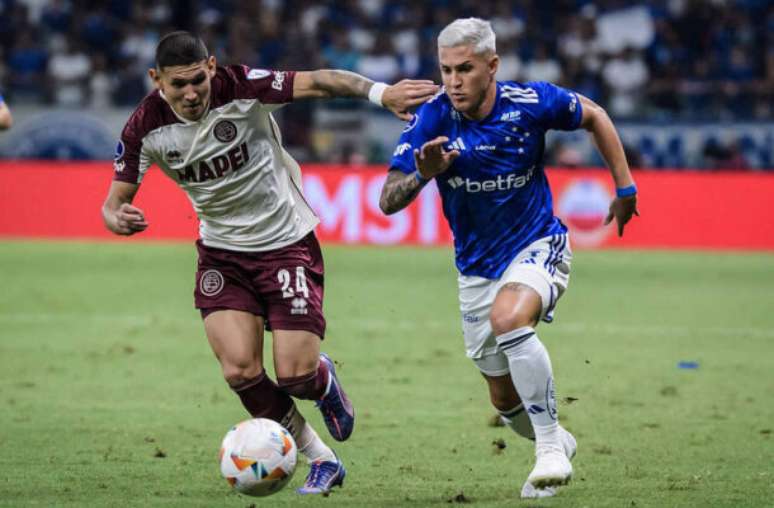 Gustavo Aleixo/Cruzeiro - Legenda: Mateus Vital leva o Cruzeiro ao ataque e recebe a marcação de Cáceres, do Lanús. No fim, 1 a 1 nesta ida da semifinal da Sul